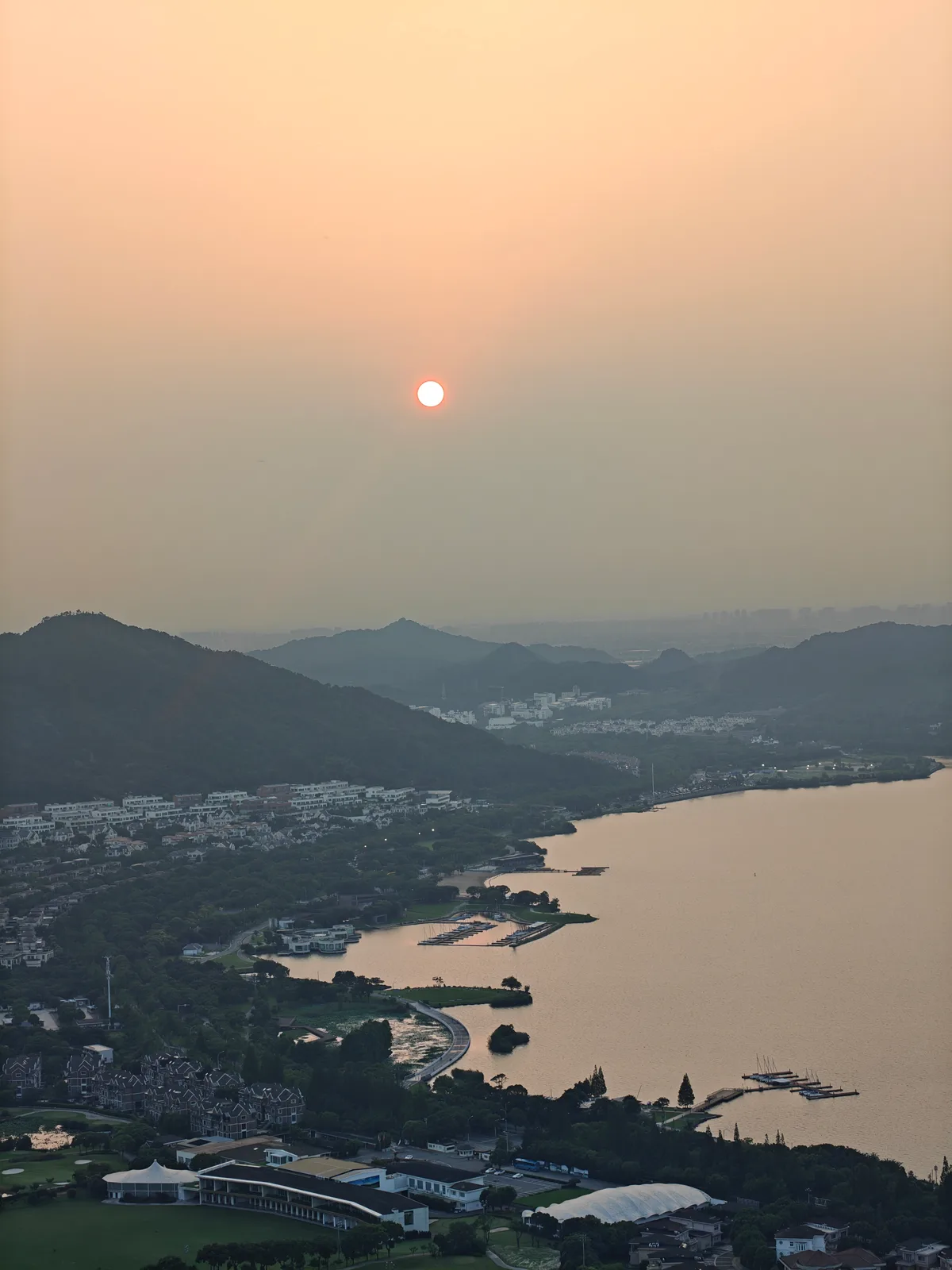 A hazy sunset over hills, a lake and a distant city